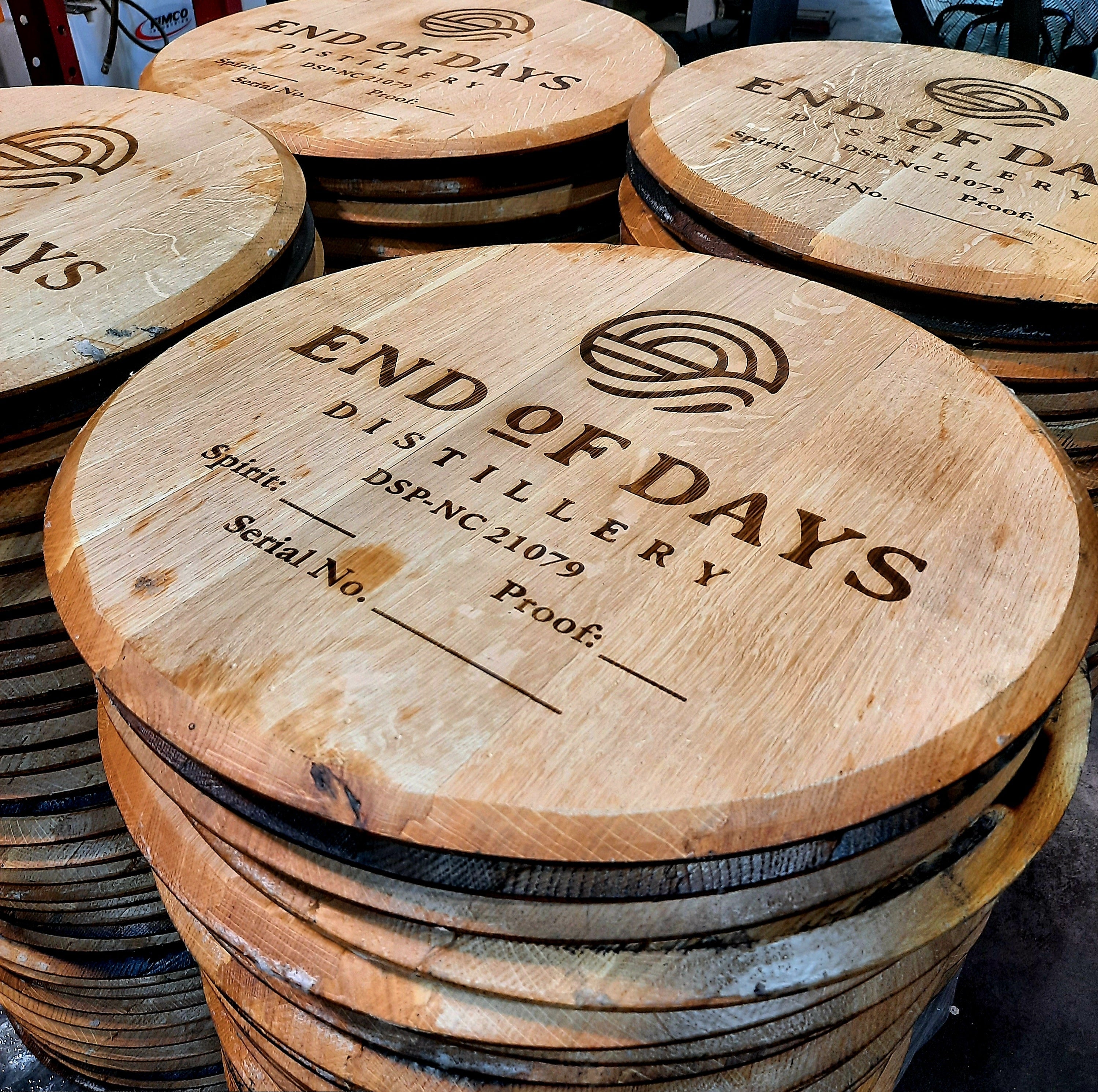 Stacked wooden barrels with engraved branding on the tops, labeled 'End of Days Distilling Co.', indicating a whiskey or bourbon barrel service.